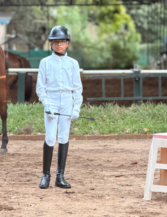 Rishabh Rajsekar in riding whites standing beside a horse at the arena